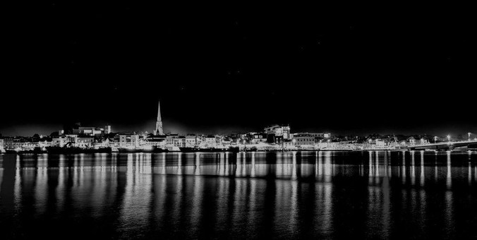 Grayscale image of Wexford town at night. In the foreground is a river which reflects the light of the town on the opposite side of the river. The town glows with lights.
