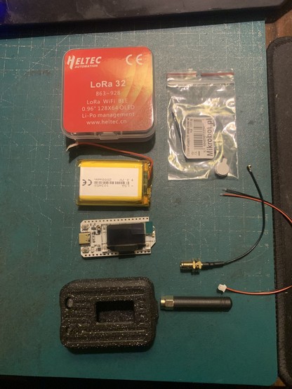 Zdjęcie elementów zestawu Meshtastic: pudełko, akumulator, modół z esp32 i displayem, obudowa, antena