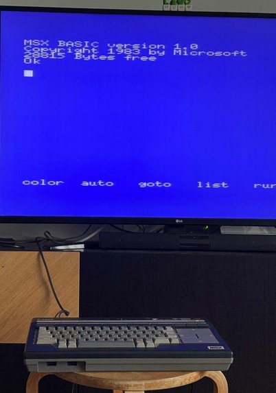 A MSX Canon V-20 from  the 80s connected to a modern TV. On the screen it displays a blue screen with the text: MSX BASIC version 1.0. Copyright 1983 by Microsoft 29915 Bytes free.