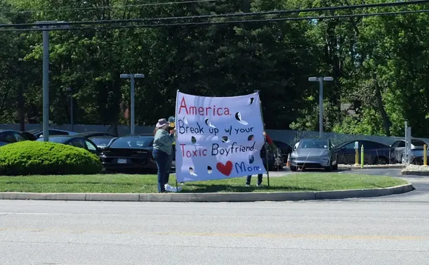 Women at a demonstration holding a large sign saying "America, break up with your toxic boyfriend. - Mom"