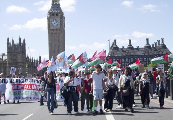 group of people with Palestinian flags on Westminster bridge, one teen carrying a boy on his back, with Big Ben in the background