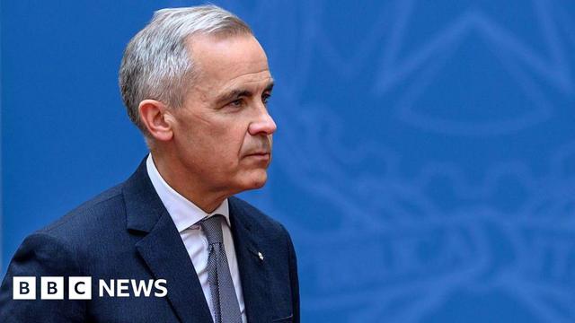 Canadian Prime Minister Mark Carney seen against a blue backdrop, wearing a darker blue suit and tie. He has a neutral expression