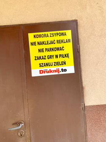 Naklejka na drzwiach: „komora zsypowa. Nie naklejać reklam. Nie parkować. Zakaz gry w piłkę. Szanuj zieleń. Druknij.to”
