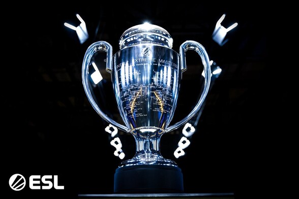 Zdjęcie trofeum - pucharu IEM Katowice, srebrny puchar z wygrawerowanym logo ESL, napisem Intel Extreme Masters i triumfatorami poprzednich edycji, ustawiony na czarnym tle