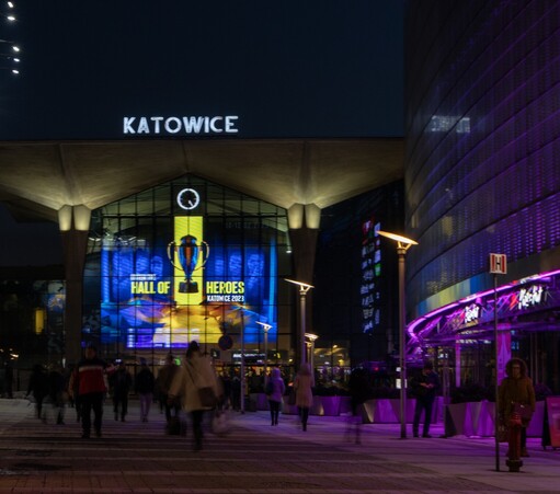 Widok na dworzec w Katowicach i reklamę IEMa wyświetlaną przez panel LED-wy na głównej ścianie dworca, na pierwszym planie ludzie idący z i na dworzec, po prawej ściana galerii handlowej