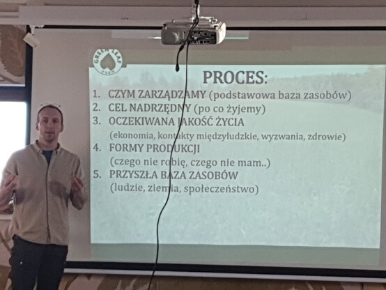 Prelegent przy ekranie, na którym wyświetlona jest strona prezentacji o procesie Holistic Management