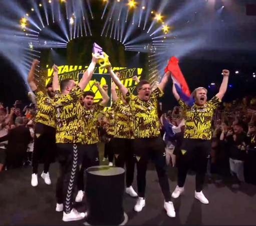 Zawodnicy Team Vitality w żółto czarnych strojach podnoszący trofeum Blast Paris Major - fioletowo-żółtą statuetkę w formie litery A, jeden z zawodników trzyma francuską flagę, wszyscy są otoczeni fanami
