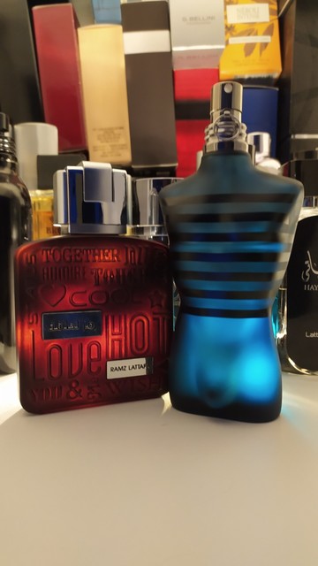 Ciemnoczerwony flakon Lattafa Ramz Lattafa i granatowy flakon Jean Paul Gaultier Ultra Male na tle podświetlonych innych flakonów perfum