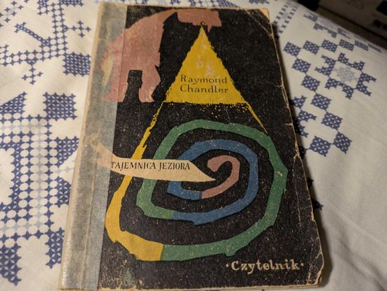 Okładka książki "Tajemnica jeziora" Raymonda Chandlera. Okłada jest stara, zniszczona, z kolorowymi zawijasami na środku i napisem "Czytelnik".